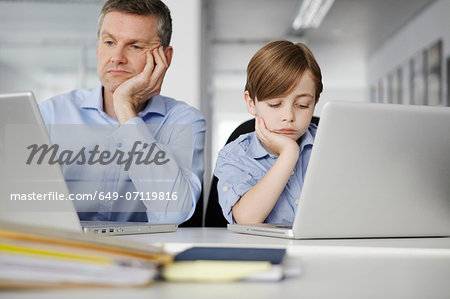 Father and son using laptops looking bored