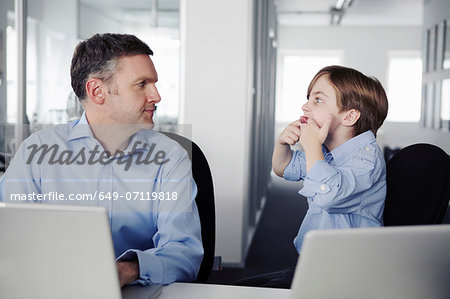 Father using laptop, son pulling faces