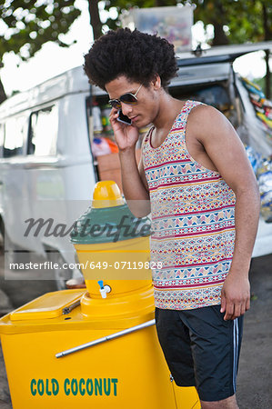 Man on cell phone with cold coconut drinks stall