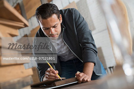 A Young Man In A Workshop Which Uses Recycled And Reclaimed Lumber Using Paper And Pen To Keep Records.