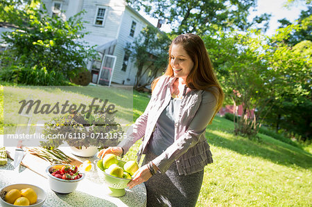 On The Farm. A Woman In A Farmhouse Garden, Preparing A Table With Fresh Organic Foods, Fresh Vegetables And Salads And Bowls Of Fresh Fruit, For A Meal.