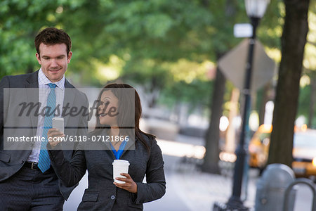 Summer. A Young Man In A Grey Suit And Blue Tie Walking With A Woman In A Suit.