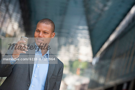 A Businessman In A Suit, With His Shirt Collar Unbuttoned. On A New York City Street. Using A Smart Phone.