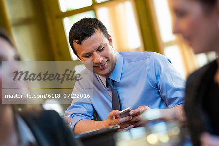 Business People. Three People Around A Cafe Table, One Of Whom Is Checking Their Phone.