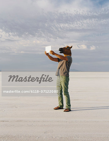 A Man Wearing A Horse Mask, Taking A Photograph With A Tablet Device, On Bonneville Salt Flats.