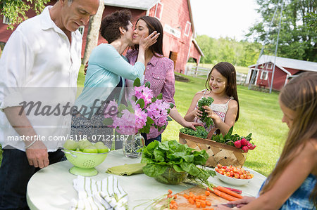 Family Party. A Table Laid With Salads And Fresh Fruits And Vegetables. Parents And Children. A Mother Kissing A Daughter On The Cheek.
