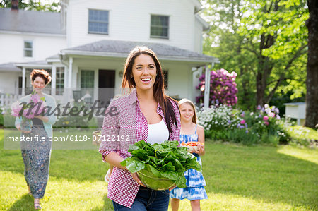 Family Party. Parents And Children Walking Across The Lawn Carrying Flowers, Fresh Picked Vegetables And Fruits. Preparing For A Party.