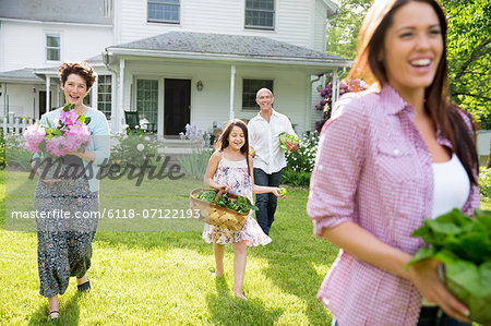 Family Party. Parents And Children Walking Across The Lawn Carrying Flowers, Fresh Picked Vegetables And Fruits. Preparing For A Party.