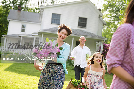 Family Party. Parents And Children Walking Across The Lawn Carrying Flowers, Fresh Picked Vegetables And Fruits. Preparing For A Party.