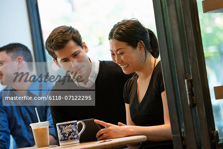 A Group Of People Sitting Around A Table In A Coffee Shop. Looking At The Screen Of A Digital Tablet. Two Men And A Woman.