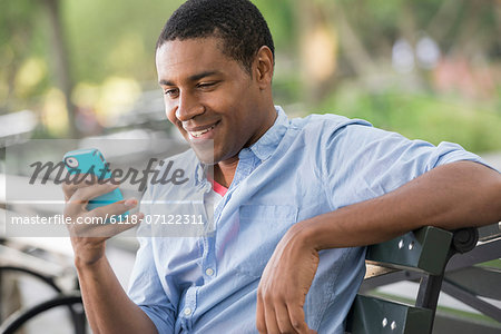 Summer In The City. A Man Sitting On A Bench Using A Smart Phone.