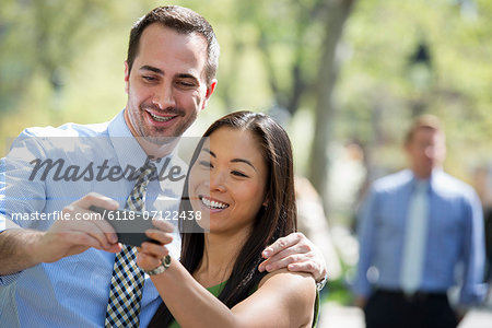 A Couple With A Smart Phone, Side By Side. A Man In The Background.
