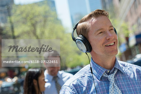 A Man Listening To Music On His Headphones. A Couple In The Background.