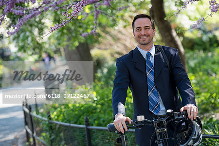 A Man In A Business Suit Astride A Bicycle With Helmet In Hand.