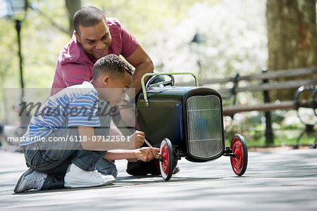 A Boy Repairing An Old Fashioned Toy Peddle Car.