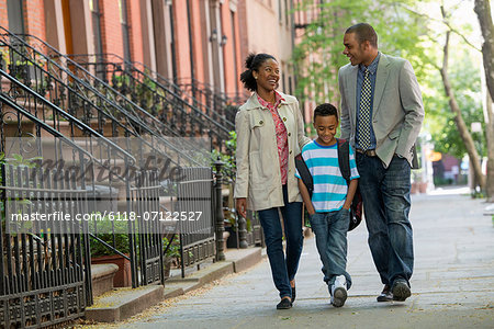 A Family Outdoors In The City. Two Parents And A Young Boy Walking Together.