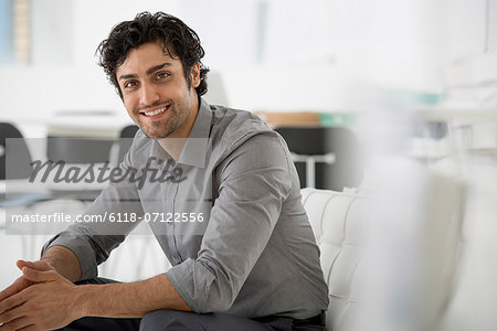 Business. A Man Seated With His Hands Clasped In A Relaxed Pose. Smiling And Leaning Forwards.