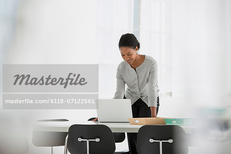 Business. A Woman Leaning Over A Desk Using A Laptop Computer.
