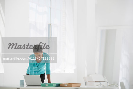 Business. A Woman Leaning Over A Desk Using A Laptop Computer.