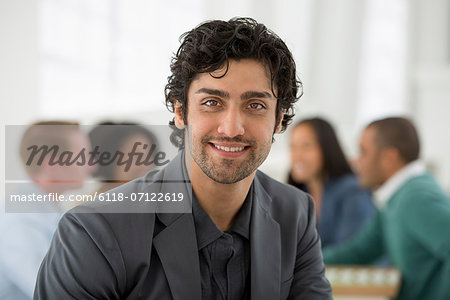 Business Meeting. A Group Sitting Down Around A Table. A Man Smiling Confidently.
