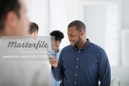 Office Interior. A Group Of People, One Man Using A Smart Phone.