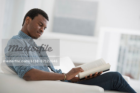 A Bright White Room Interior. A Man Sitting Reading A Book.