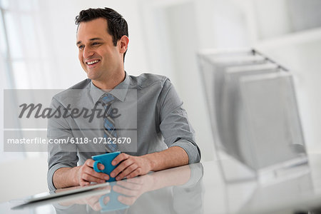 Office Interior. A Man Seated At A Table. A Digital Tablet.