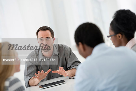 Office Interior. A Group Of Four People, Two Men And Two Women, Seated Around A Table. Business Meeting.