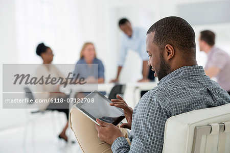 Office Interior. Meeting. One Person Seated Separately, Using A Tablet Computer. Holding A Digital Tablet.