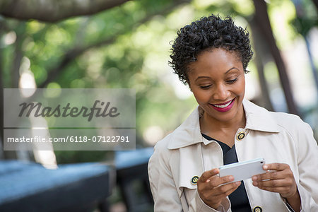 City. A Woman Outdoors In The Park, Checking Her Smart Phone.