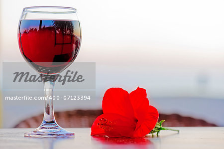 Glass of red wine with a flower at sunset.