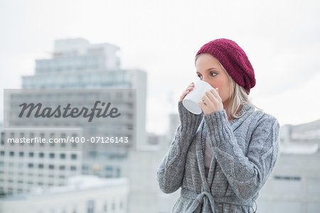 Peaceful gorgeous blonde drinking coffee outdoors on urban background
