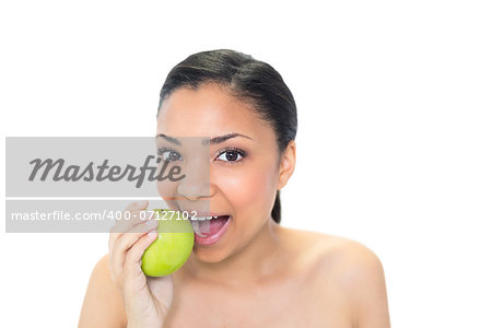 Playful young dark haired model eating a green apple on white background