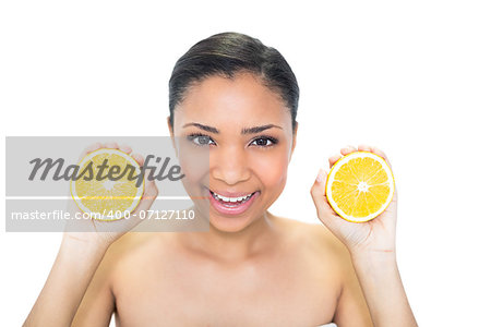 Joyful young dark haired model holding orange halves on white background