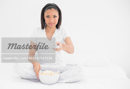 Relaxed young dark haired model eating popcorn in bright bedroom