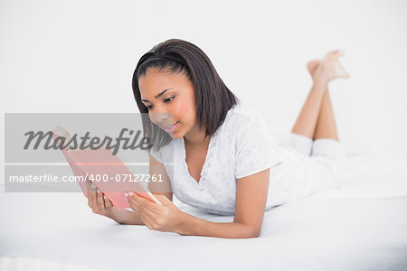 Concentrated young dark haired model reading a book in bright bedroom