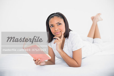 Dreamy young dark haired model reading a book in bright bedroom