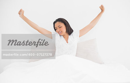 Exhausted young dark haired model stretching in her bed in bright bedroom