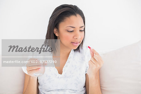 Unsmiling young dark haired model taking medication in bright bedroom