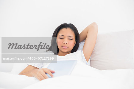 Sleepy young dark haired model holding a tablet pc in bright bedroom