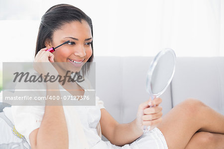Seductive young dark haired woman in white clothes applying mascara in a living room
