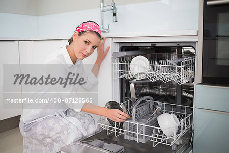 Serious charming woman using dish washer in bright kitchen