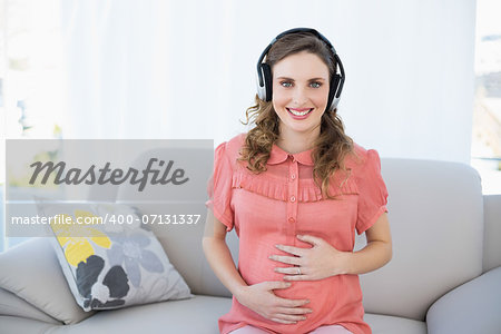 Content pregnant woman relaxing listening to music sitting on couch smiling at camera