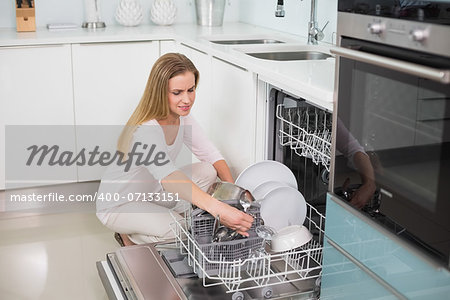 Happy gorgeous model kneeling behind dish washer in bright kitchen