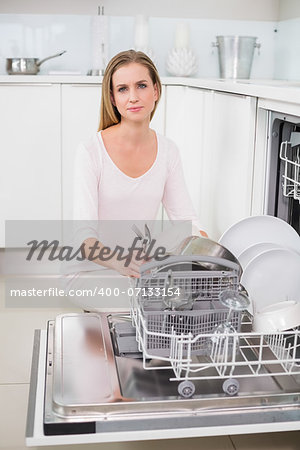 Serious gorgeous model kneeling behind dish washer in bright kitchen