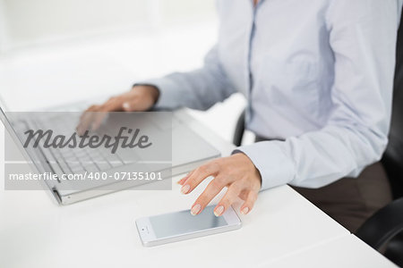 Side view mid section of a businesswoman using laptop and cellphone in the office