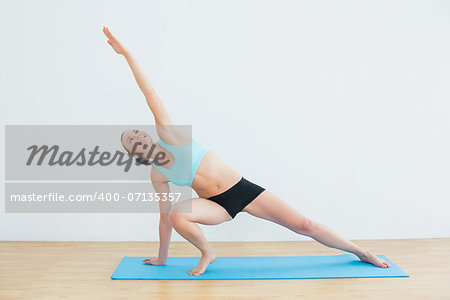 Full length of a slim young woman doing the side plank yoga pose in fitness studio