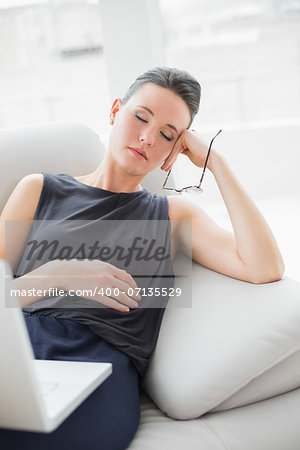 Beautiful well dressed young woman resting on sofa while using laptop at home