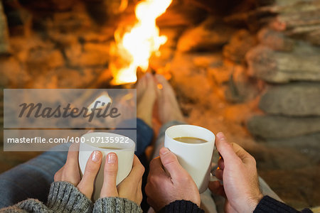 Close up of hands holding coffee cups in front of lit fireplace
