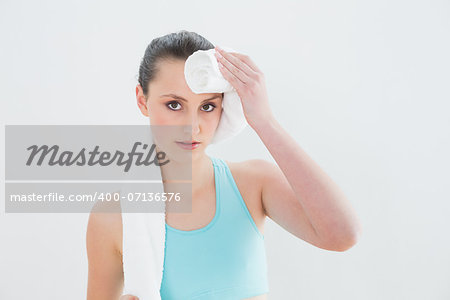 Close up of a young woman wiping sweat with towel against wall at fitness studio